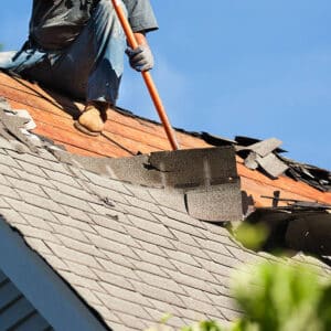 Roofer tearing off shingles on roof